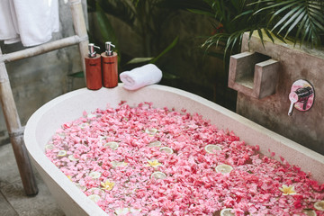 Bath tub with flower petals, towel and beauty products