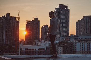 Brutal and musculine man in t-shirt and hat ginst evening cityline with bulding