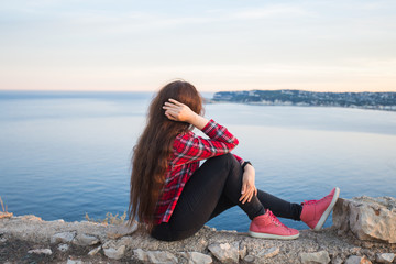 Travel, adventures and loneliness concept - A girl sits on the edge of the cliff and looking the sea