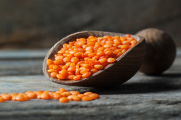 Red lentils in wooden shovel on wooden background. Uncooked red lentil legumes, herbaceous plant (Lens culinaris)