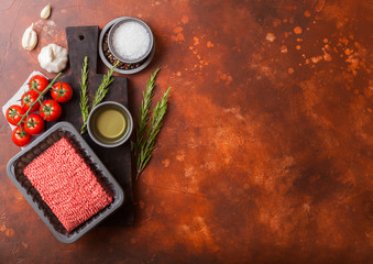Tray with raw minced homemade beef meat with spices and herbs. Top view and space for text. On top of rusty kitchen table background. With pepper salt and garlic.