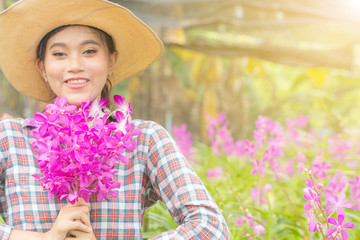 A woman gardener wearing a plaid shirt wearing a hat is holding a pink orchid in his hand. And was smiling happily. In the orchid garden