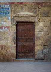 Fototapeta na wymiar Old wooden door framed by bricks stone wall at the courtyard of al Razzaz historic house, Darb al Ahmar district, Old Cairo, Egypt