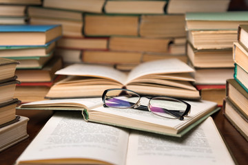 Open books and glasses on wood desk in the library room with blurred focus for education background and back to school concept