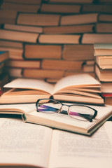 Open book and glasses on wood desk in the library room with blurred focus for education background...
