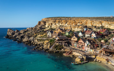 Beautiful view on home of Popeye. Village with many colorful houses in a comic style. Located in the Anchor Bay in Malta. Blue sky, Sea and cliffs in foreground. Popeye Village, mellieha, Malta.