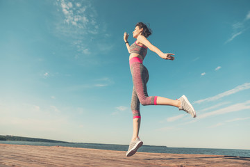 Obraz premium Sporty young girl in the morning on pier in jump, practicing yoga. Woman do gymnastics outdoors. Health and Yoga Concept. Female lifestyle meditation for fitness lifestyle the nature background