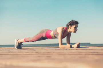 Sporty young girl in the morning on the pier on seashore, practicing yoga. Woman do gymnastics outdoors. Health and Yoga Concept. Female meditation for fitness lifestyle the nature background