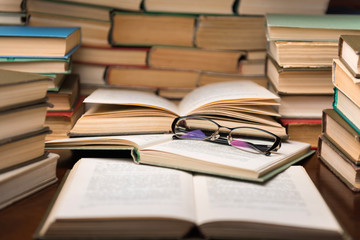 Old open books in library, stack piles of literature text archive on reading desk in school study class room, background for education learning concept. Narrow depth of field