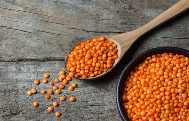 Red lentils in wooden spoon on wooden background. Uncooked red lentil legumes, herbaceous plant (Lens culinaris) in bowl