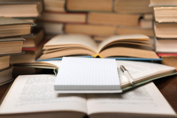Education learning concept with open book and notebook on the table. Stack piles of books on reading desk and glasses in bookshelves background