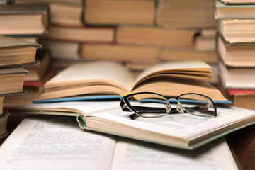 Open book and glasses on wood desk in the library room with blurred focus for education background...