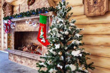 Fireplace with Christmas tree and red gift sock near wooden wall