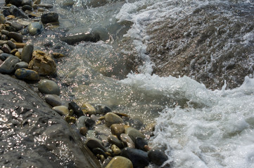 pebble stones on the sea beach, the rolling waves of the sea with foam
