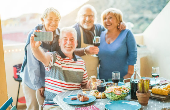Happy seniors friends taking a selfie photo with smartphone camera at barbecue dinner in house terrace - Focus on mobile cell phone