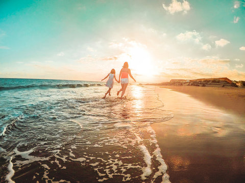 Mother And Daughter Running Inside The Water On Tropical Beach