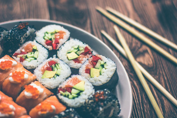 Sushi roll with salmon, cucumber, avocado, red caviar with chopsticks. Close up