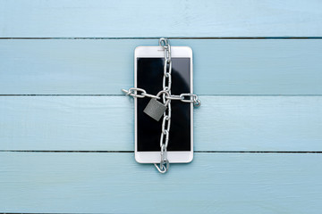 The smartphone is associated with a chain with a lock, on a wooden table
