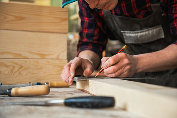 The worker makes measurements of a wooden board with ruler.