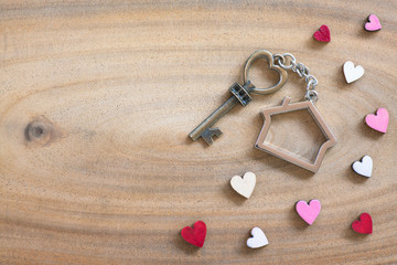House key in heart shape with home keyring on wood background decorated with mini hearts - 254207243