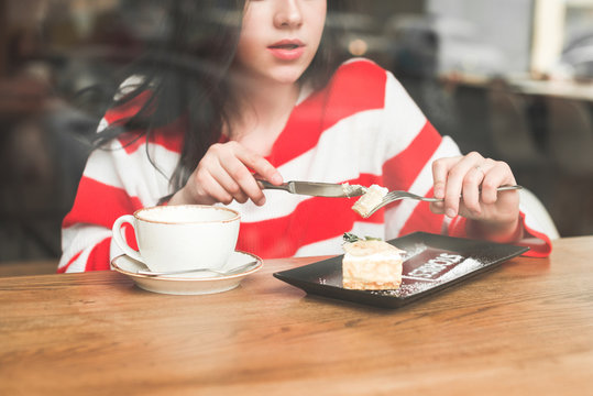 Girl Eating A Piece Of Cake In A Restaurant Close Up.Attractive Girl Sits In A Cafe With A Fork With A Cake And A Knife In His Hands And Eats Dessert.Lady Eats A Cheesecake In A Cafe And Drinks Coffee