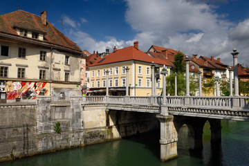 Fototapeta na wymiar Columns on the Plecnik designed Cobblers Bridge over the Ljubljanica river with old and renovated houses Ljubljana Slovenia