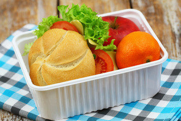 Healthy school lunchbox containing roll with cheese, lettuce and tomato, red apple and mandarine