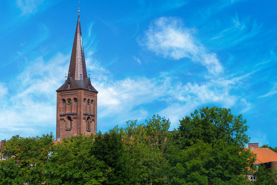 Steeple of the church of ploen in germany towering over trees. Nice view on the church tower on a sunny light cloudy day.