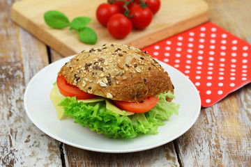 Mixed grain roll with cheese, lettuce and tomato on vintage plate