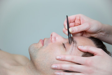 Man getting his eyebrows shaped with a tweezer. Beauty skin care for men. 