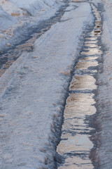 winter road covered with snow and ice with puddles and ruts