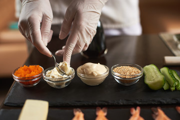 Closeup of chef hands preparing components for cooking rolling sushi at restaurant.