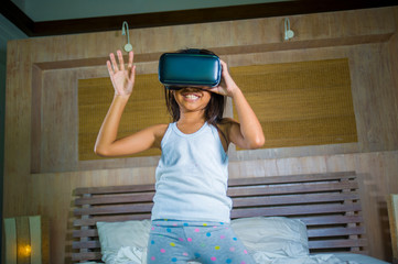 lifestyle portrait of young happy and excited female child wearing VR goggles device headset playing virtual reality simulation game enjoying an amazing experience