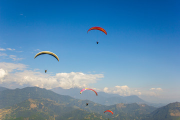 a group of paragliders on colored parachutes in a clear blue sky over a mountain valley