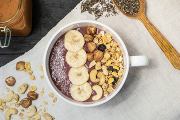 Bowl of fruit smoothie, nuts and banana, top view. Flat lay of an acai bowl with cereals, cashews and hazelnuts on vintage rustic table
