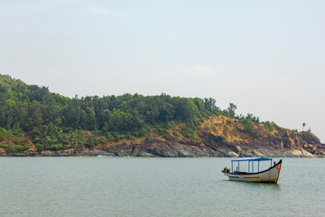 empty pleasure boat with a roof in the ocean against a rocky shore with green trees, view from the sea