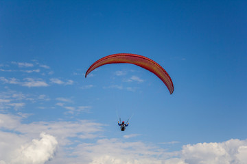 paraglider on a red parachute flies in a clear blue sky with white clouds aerial view