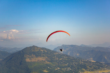 paraglider on a red parachute flies over a green mountain valley under a clear blue sky aerial view
