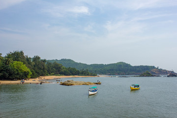 sea bay with pleasure boats on the water, against the background of the green forest on the sandy beach and people resting