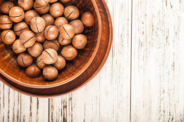 Macadamia nuts on a wooden plate on a white textural table close up and copy space
