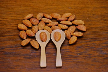 Two spoon with an almond in each spoon placed on pile of almonds on wooden background.
