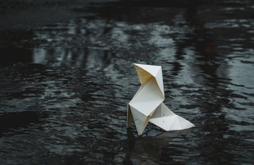 Origami paper figure on the background of a gloomy city street and puddles