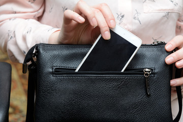 woman's hand pulls out a white smartphone from a black handbag