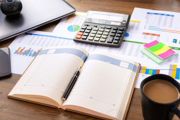 Open leather notebook, laptop, cup of coffee, calculator, graphs, data and drawings on the working office desk. Business and Finance.