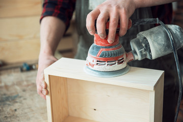 Worker grinds the wood box of angular grinding machine