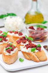 Bruschetta with sun dried tomato, feta and philadelphia cheese and basil on a ceramic plate, vertical