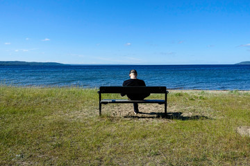Naklejka na ściany i meble JÖNKÖPING, SWEDEN Man alone on bench on shore of Lake Vättern