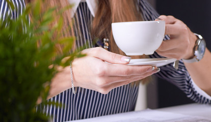 Coffee cup in businesswoman's hand. Young woman working with documents and laptop close-up.