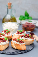 Bruschetta with sun dried tomato, feta and philadelphia cheese and basil on stone plate, vertical