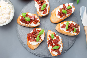 Bruschetta with sun dried tomato, feta and philadelphia cheese and basil on stone plate,...